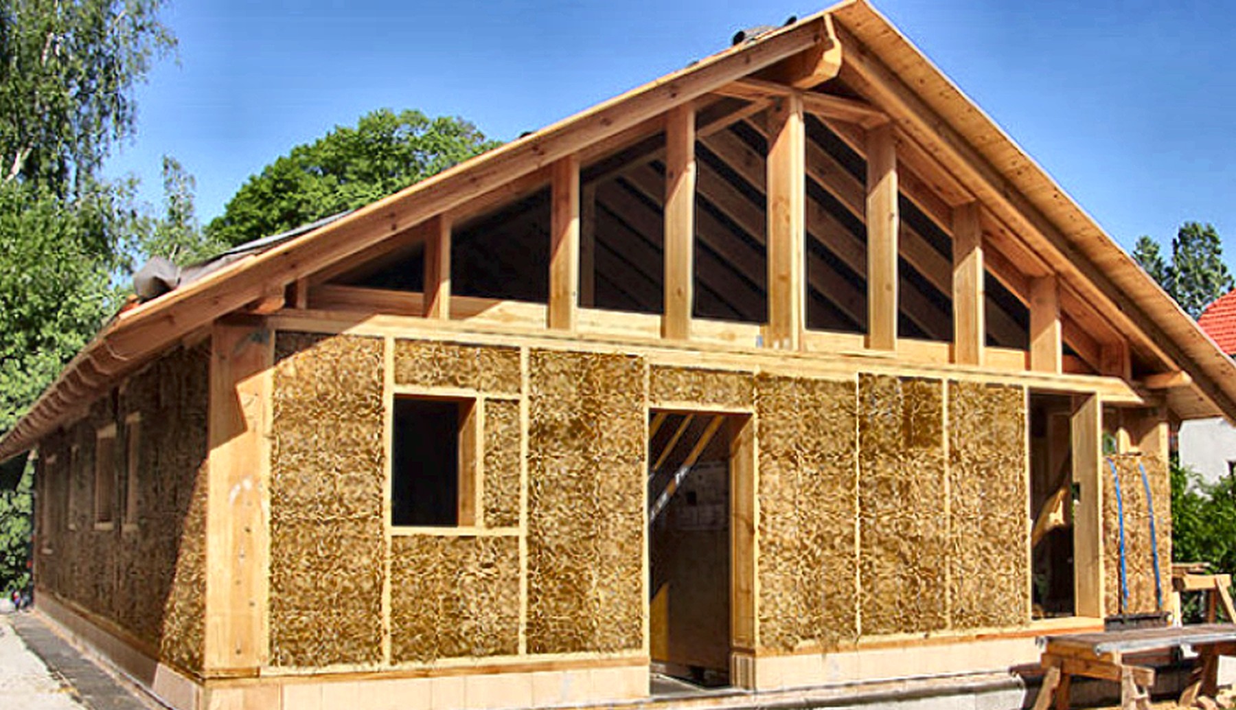 A compressed-straw home with a timber frame set against wooded hills